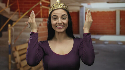 Hispanic woman wearing a crown makes funny faces at a construction site with red bricks and indoor...