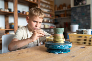 Focused boy painting ceramic cup at home pottery studio
