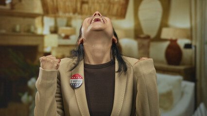 Young hispanic woman indoors wearing 'i voted' badge smiles with closed eyes, symbolizing joy and...