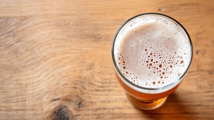 Glass of beer with foam head resting on wooden table