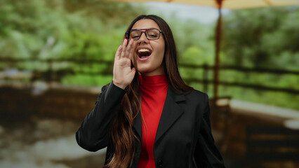 Young hispanic woman shouting with joy in a lush green outdoor park setting, emphasizing vibrant...