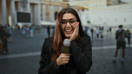 Woman reporter smiling confidently with microphone in vatican st peter's square under clear sky...