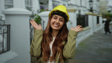 Woman smiling with hands over face in outdoor urban street setting wearing a yellow safety helmet...