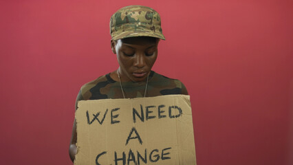 Young woman soldier in camouflage uniform holding a cardboard sign in studio; protest determination.