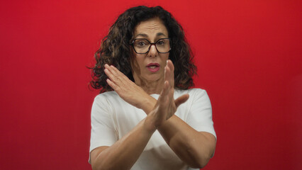 Middle-aged hispanic woman gesturing against red background, conveying refusal or stop with hands...