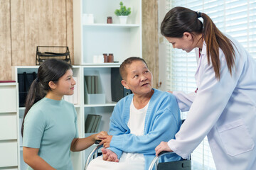 Asian doctor and young woman warmly interact with elderly patient in wheelchair, offering...