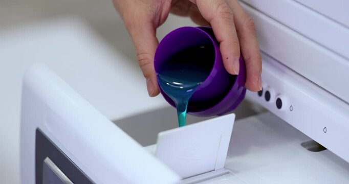 Woman pours liquid laundry detergent into compartment of washing machine, close-up