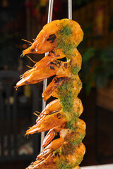 Grilled shrimps on a skewer with herbs and spices, hanging in a restaurant setting