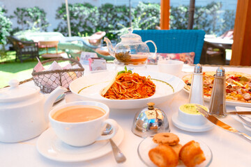 Al fresco brunch table set-up with Italian food. Cafe dining with seafood pasta, Capricciosa pizza, bread basket, butter, cup of coffee, pot of tea