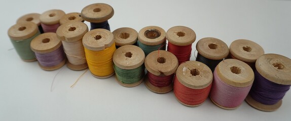 A row of vintage wooden spools with threads of different colors, neatly laid out on a white...