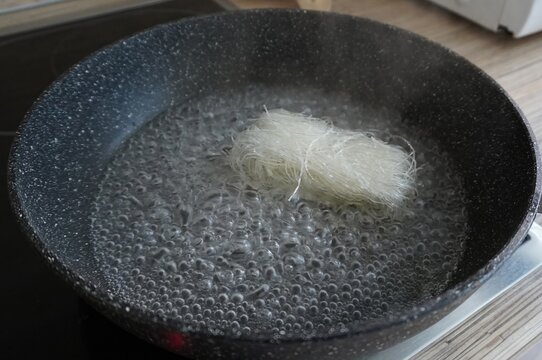 Water is boiling in a saucepan, into which a bunch of glass noodles (funchosa) is dipped, the cooking process is on the stove.
