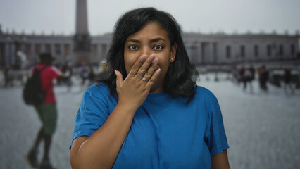 African american woman in blue shirt holds hand to lips gesture while looking forward in vatican...