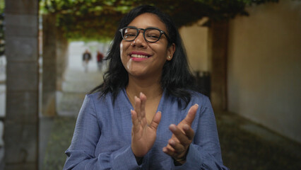 Woman clapping bare hands in building corridor lined with climbing vines and stone pillars;...