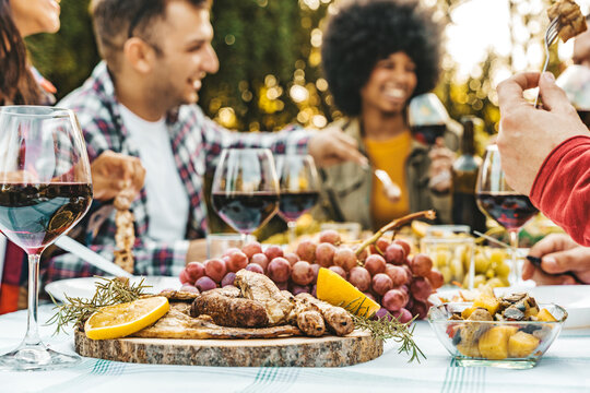 Group of young people having fun drinking red wine on balcony rooftop bbq dinner party - Happy multiracial friends eating barbecue food at restaurant terrace - Food and drink life style concept