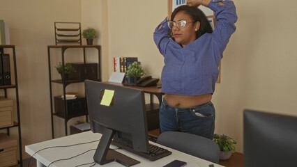 Woman stretches arms over computer monitor at office desk inside building; work break relaxation...