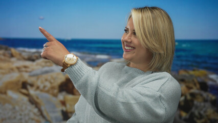 Blonde woman pointing finger with smiling face wearing sweater and wooden watch in studio; optimism.