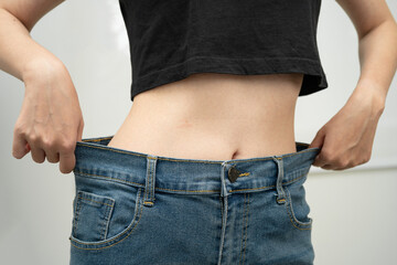 Young Asian woman losing weight wearing loose pants in oversize jeans.