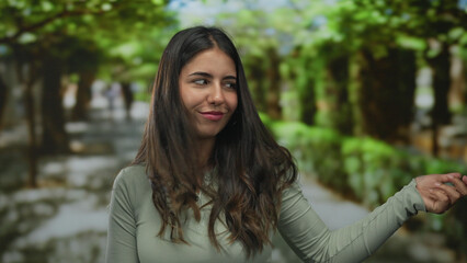Young hispanic woman strums guitar gesture with hands along leafy green forest path under sunlight;...
