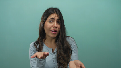 Young hispanic woman beckons open palm for money in studio against green wall, making beckoning...