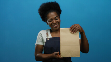Woman waitress holds paper bag for takeaway over a blue background showing a happy expression