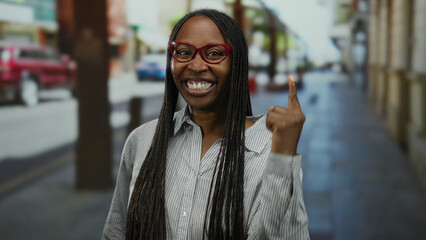 Woman smiling outside in urban street with red glasses curly hair against city backdrop showcasing...