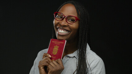 Woman smiling holding danish passport against black background wearing red glasses and striped shirt showcasing joyful expression.