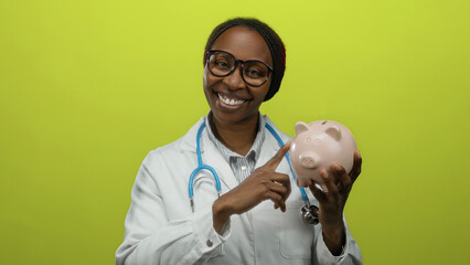 Woman wearing a white coat pointing at a piggy bank against a yellow background, demonstrating...