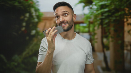 Hispanic man recording voice message on smartphone outdoors in a lush green park creating a vibrant...