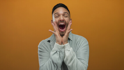Young man expressing joy against vibrant orange background wearing casual gray shirt while smiling...