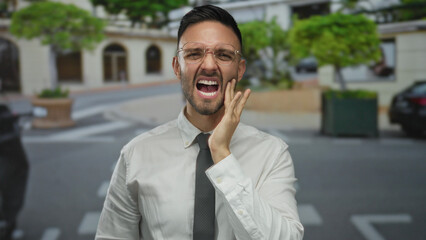 Young man in white shirt expressing discomfort on an urban city street, capturing a moment of...