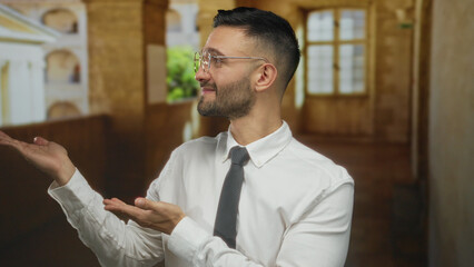 Young man with glasses points to the side inside historic university campus building wearing formal shirt and tie