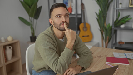 Obraz premium Young man thinking in cozy living room with guitar and plants surrounding him at home office setup
