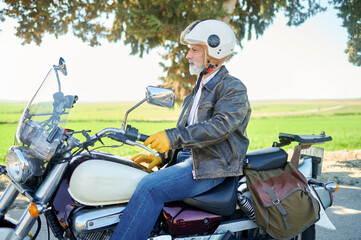 Stylish senior man with helmet and gloves riding a motorcycle on a country road