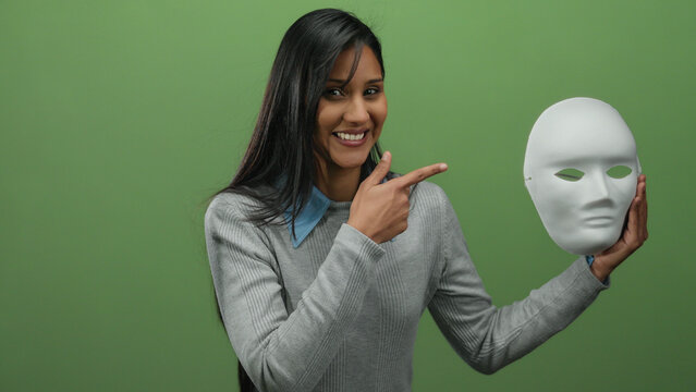 Woman smiling holds white mask pointing isolated green background happy expression media concept