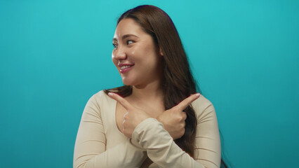 Fototapeta premium Hispanic woman pointing both index fingers crossed at chest in studio setting while smiling; rejection.