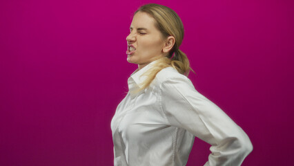 Woman grimacing in pain with hand on back against a vibrant pink background, highlighting...