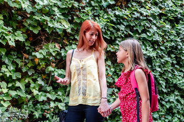 Mother and daughter holding hands and talking on their way to school