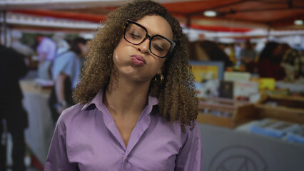 Woman puffs cheeks while blowing air in a crowded street market souvenir stall, pressing lips...