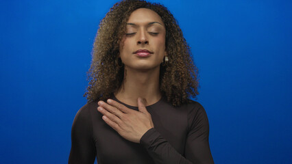 Woman raising her palm and placing her other hand on chest in a blue studio setting; pledge...