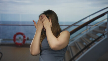 Young woman covers mouth with trembling hands and clings to railing on building; fear vulnerability.