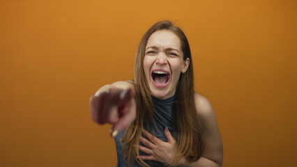 Young caucasian woman pointing finger at viewer with open mouth and chest clutch gesture in studio;...