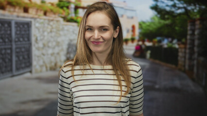 Young woman with a slight smirk pointing finger to head in striped shirt on a busy city street...