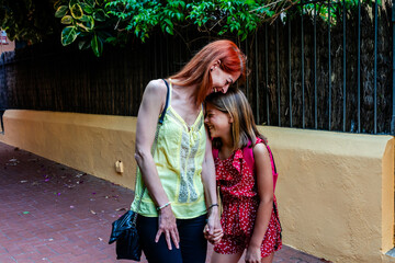 Mother and daughter holding hands and smiling on their way to school