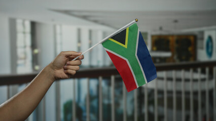 Person holding south african flag inside a hotel, showcasing national pride with focus on hand and...