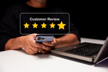 A person holding a smartphone near a laptop with a five-star customer review icon displayed.