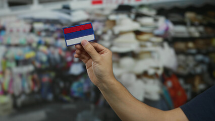 Man holding embroidered russian flag patch against market background, showcasing street vendor...