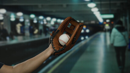 Man wearing baseball glove holds ball at indoor train station, capturing an unexpected sports...