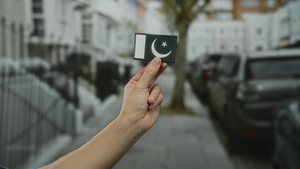 Hand of a man holding a pakistani flag embroidery on a vibrant city street outdoors.