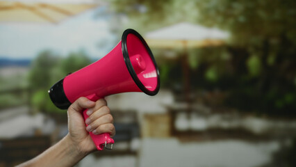 Man holding pink megaphone in outdoor terrace cafe with blurred background, highlighting city...