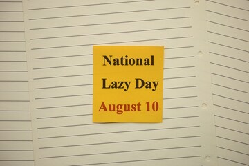 Yellow paper note with words National Lazy Day August 10 lying on lined notebook pages